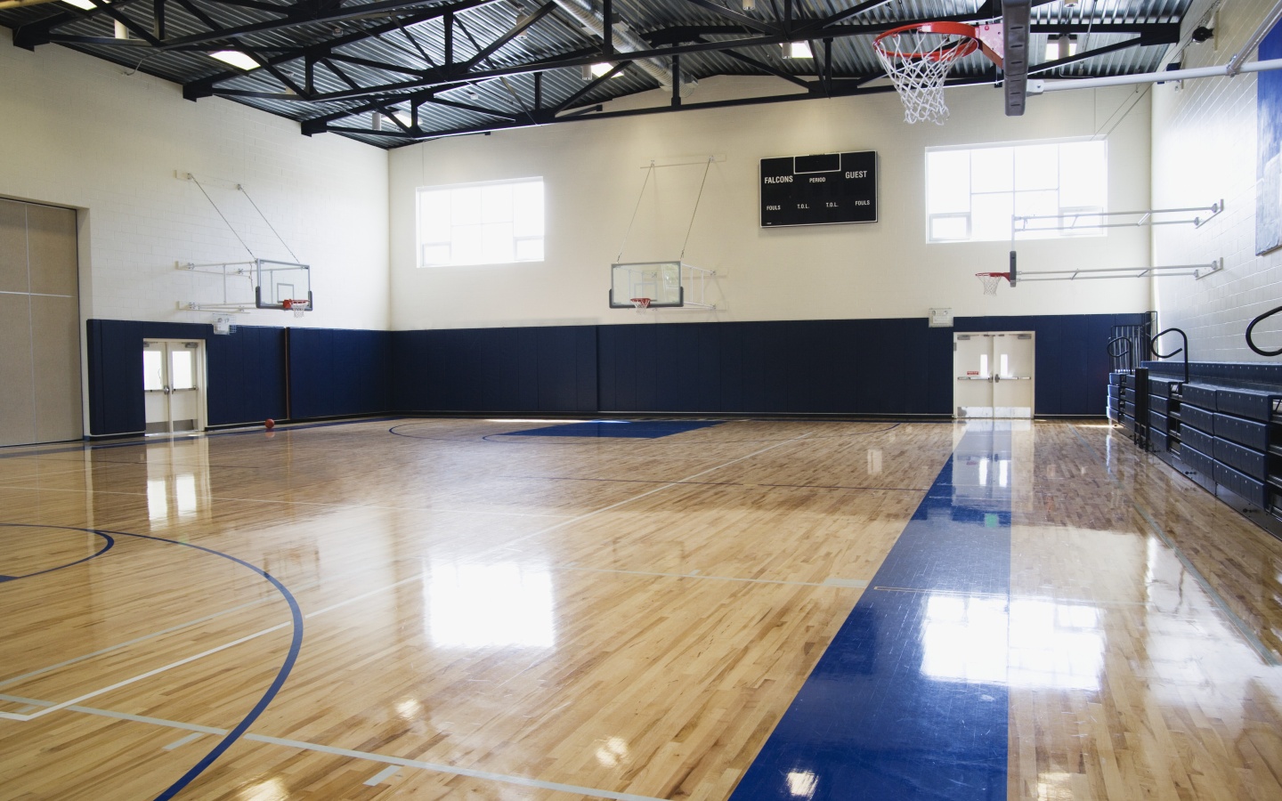Connor<sup>®</sup> Sports hardwood gym flooring with maple basketball court, blue game lines, and retractable basketball hoops in a high school gymnasium