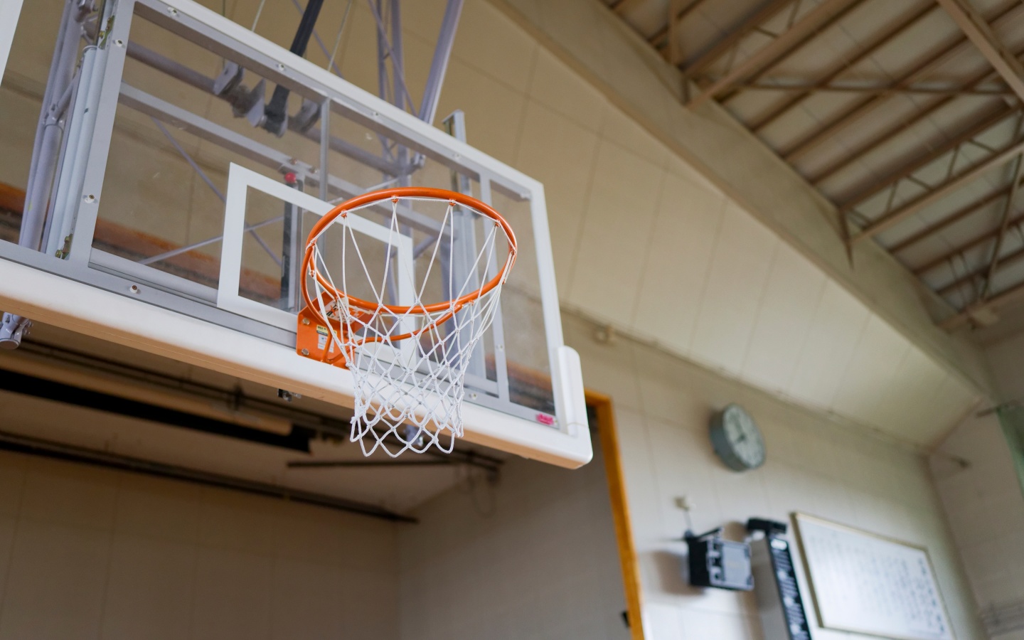 Close-up view of an indoor gymnasium basketball hoop, orange rim, white net, and clear backboard mounted inside a sports facility.